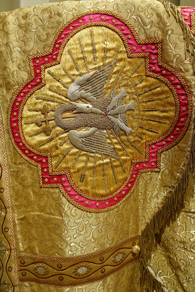 Nahaufnahme eines Priestergewänders mit goldener und roter Stickerei gegen einen Wandhintergrund.