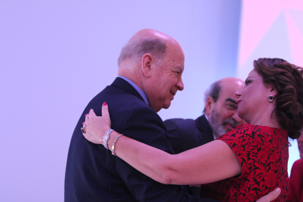 Zwei Menschen umarmen sich auf einer Bühne, andere sind in der Nähe, der Mann trägt ein Armband.