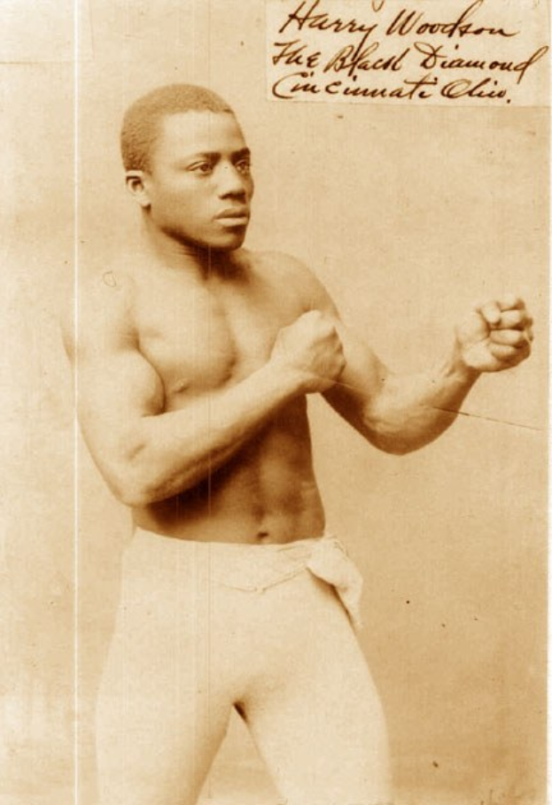 Ein Schwarz-Weiß-Foto eines Mannes im Boxring mit Handschuhen und Shorts, der entschlossen dasteht.