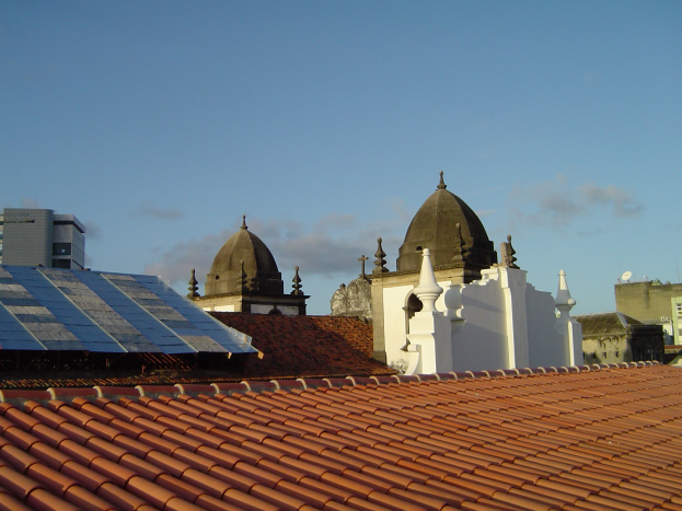 Stadtlandschaft mit einigen Gebäuden im Vordergrund, einem blauen Himmel im Hintergrund und Solarpanelen auf dem Dach eines Gebäudes.