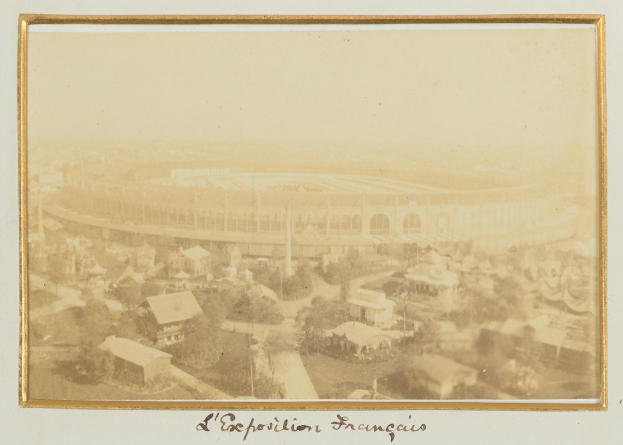 Schwarzes und weißes Foto eines Stadions in einer städtischen Umgebung, umgeben von Gebäuden, Bäumen und Strommasten, mit Text am unteren Rand.